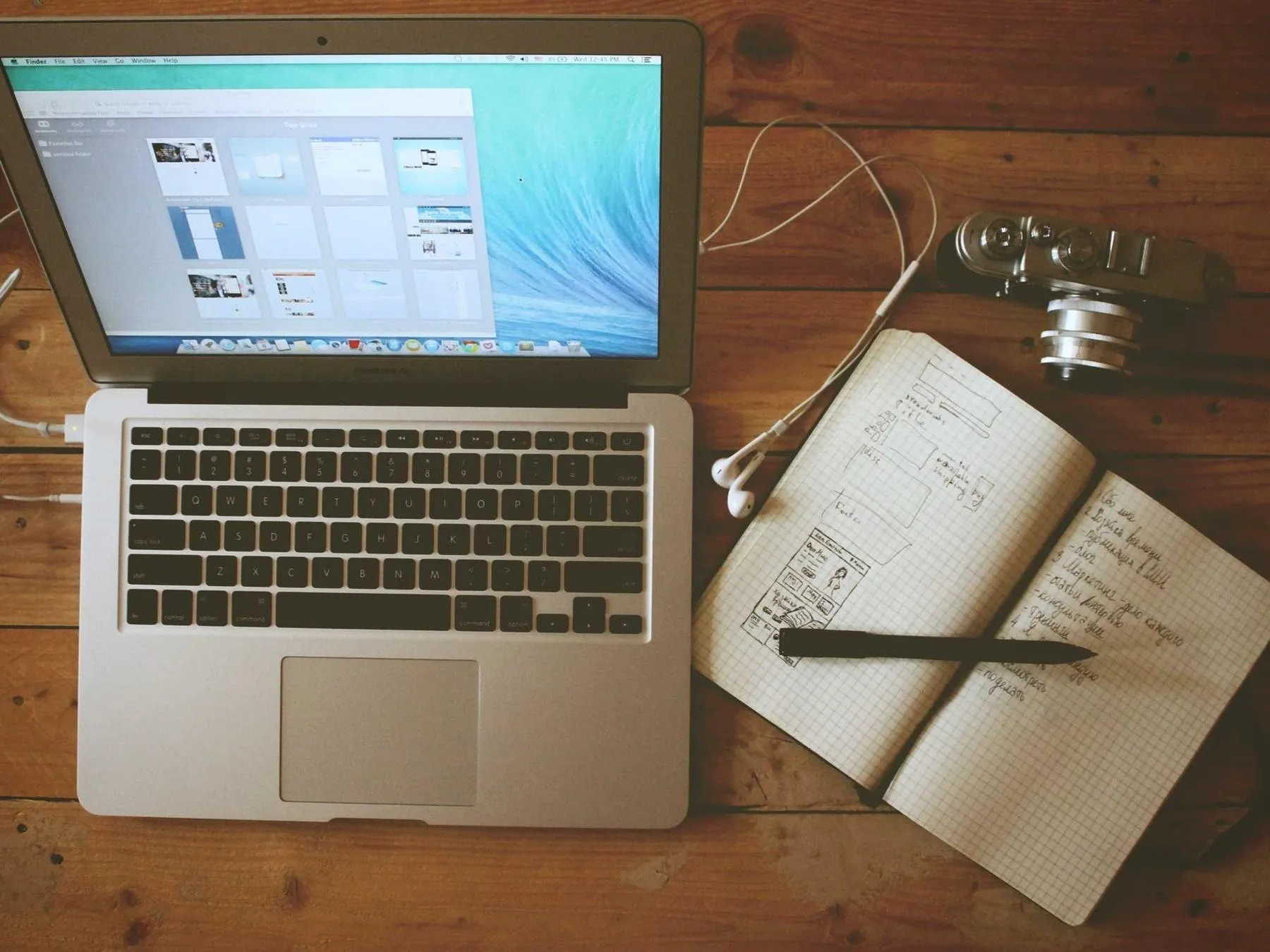 An open laptop beside a hand-sketched notebook and a pair of headphones on a wooden desk