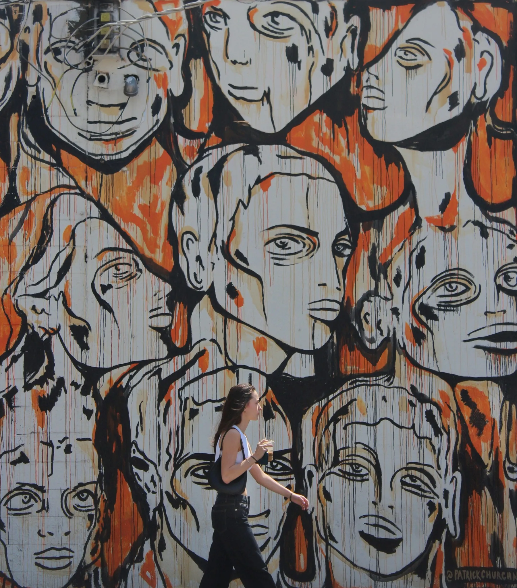 A person walking past a mural of painted faces